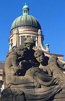 
   Skulptur einer männlichen Dreiergruppe,   
   im Hintergrund das Oberlandesgericht   
