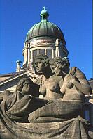 
   Skulptur einer weiblichen Dreiergruppe,   
   im Hintergrund das Oberlandesgericht   
